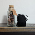 Glass jar with cork lid and black drawstring bag on a wooden surface.