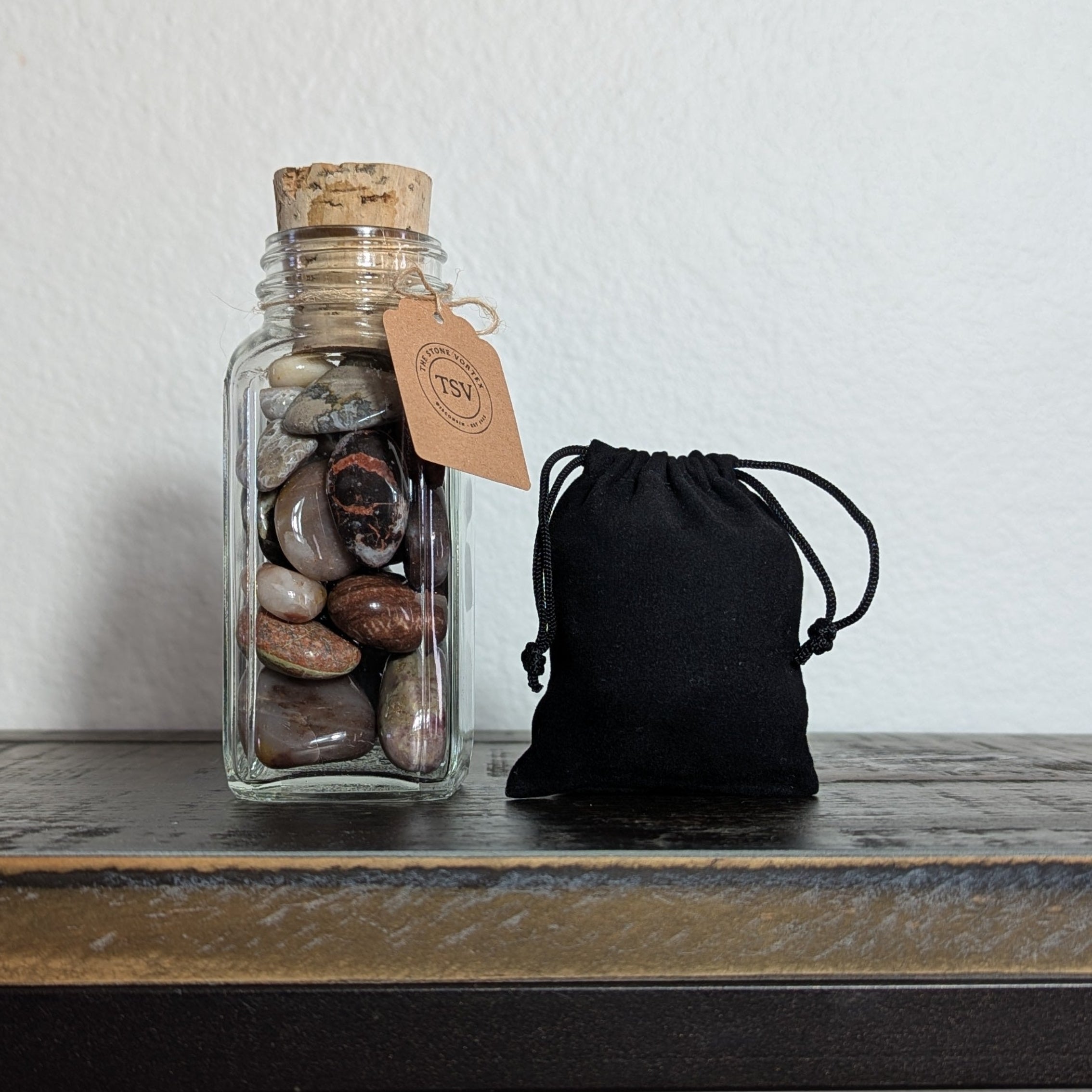 Glass jar with cork lid and black drawstring bag on a wooden surface.