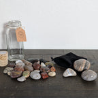 Collection of stones on a wooden surface with a glass jar and candle in the background.