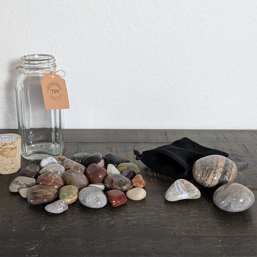 Collection of stones on a wooden surface with a glass jar and candle in the background.