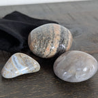 Three stones on a wooden surface with a black drawstring bag.