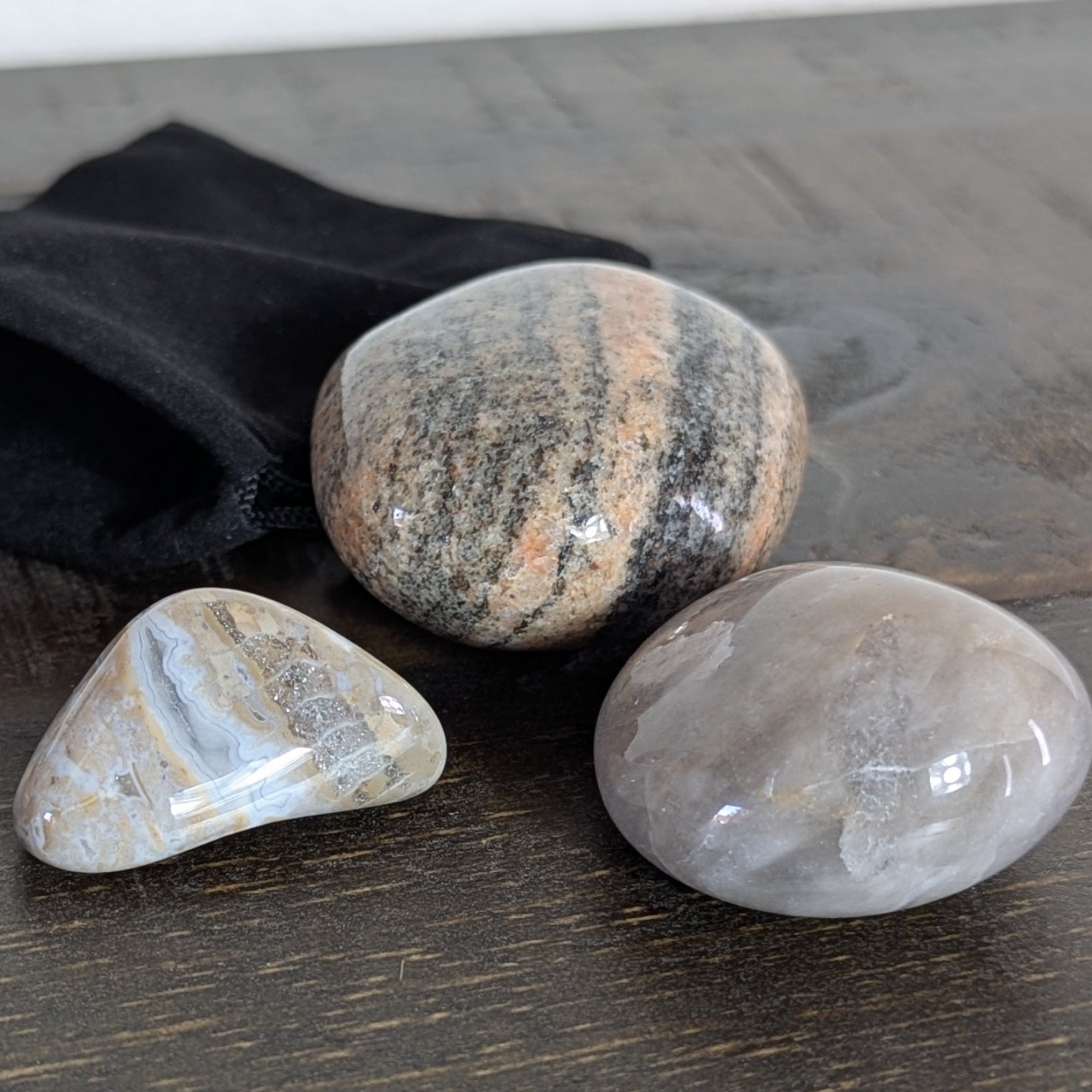 Three stones on a wooden surface with a black drawstring bag.