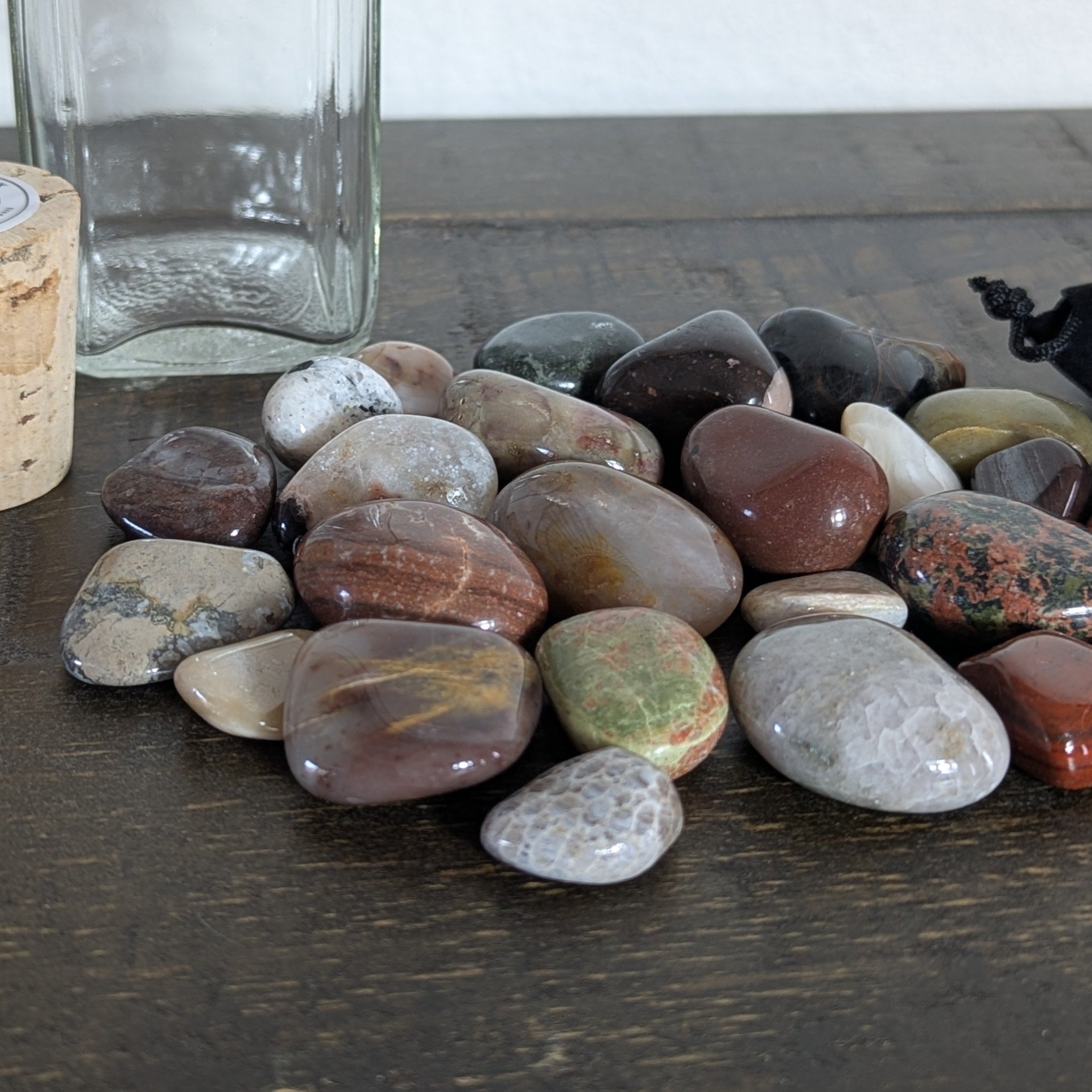 Collection of multicolored stones on a wooden surface with a clear glass jar and cork in the background.