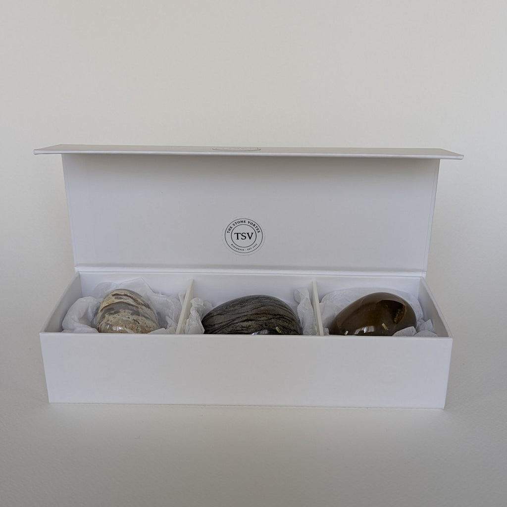 Open white box containing three stones on a light gray background